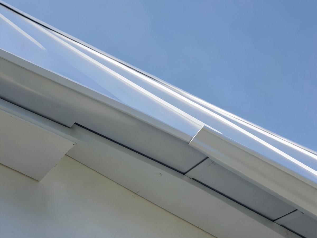 Detail of a silver standing seam roofline meeting a clean fascia and gutter